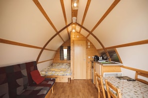 A cozy attic bedroom with a bed, a sofa, a small kitchenette, and a window.