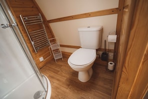A small, clean bathroom with a wooden floor, a white toilet, a metal towel rack, and a shower area.