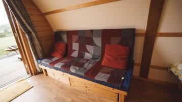 A wooden bench with a quilted backrest and cushions, positioned in a room with wooden beams and a wooden floor.