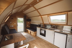 Een kleine keuken met een inbouwoven, magnetron en spoelbak, houten vloeren, en een raam met uitzicht op een mooi landschap.