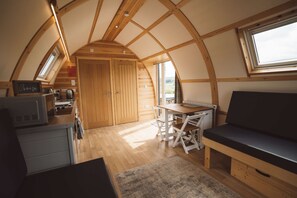 A cozy, compact kitchen with wooden cabinets, a dining table, and a bench. - Wooden Cosy Cabin with Hot Tub in Mid Wales (Llanbrynmair)