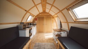 A compact kitchen with wooden cabinets, a microwave, and a sink. There are two seating areas with benches and a small table. - Wooden Cosy Cabin with Hot Tub in Mid Wales (Llanbrynmair)