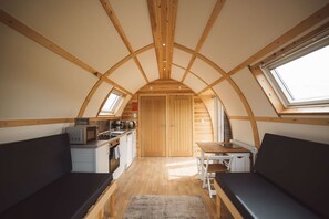 Une cuisine compacte avec des meubles en bois, un four à micro-ondes et un évier. L’espace comprend deux coins salon avec des bancs et une petite table.