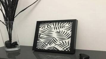 Een lijstwerk met een bladpatroon, een vaas met takken en enkele stenen op een reflecterend oppervlak.