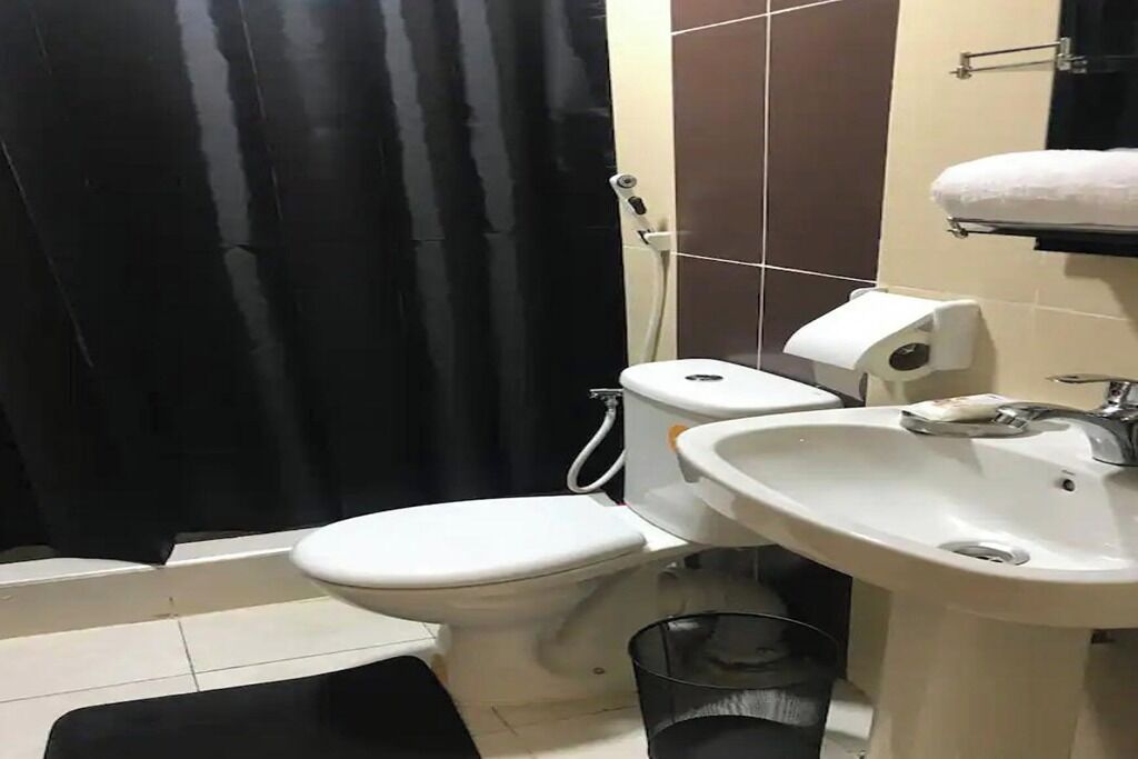 A bathroom with a toilet, bidet, sink, and a trash bin.
