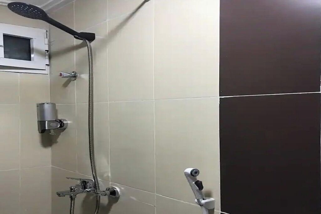 A shower area with a handheld showerhead, a wall-mounted faucet, and a handheld shower head.