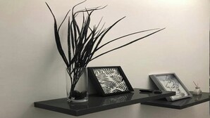 A black shelf with a vase of tall, thin plants and two framed artworks. -  5-beds apartment with AC, WiFi, Smart TV # Meknes (Meknes)