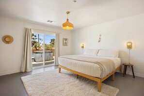 A bedroom with a bed, a window with curtains, a ceiling light, and a small stool.
