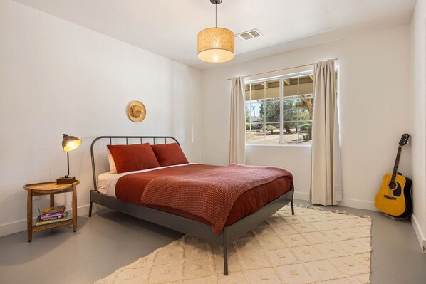 Une chambre à coucher avec un lit, une lampe de chevet, une guitare et une fenêtre avec des rideaux.