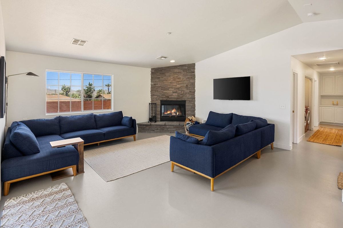 Una sala de estar con dos sofás, una chimenea, un televisor y un ventanal grande.