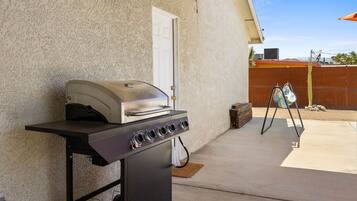 A portable grill with a control panel, set up on a concrete patio with a house in the background.
