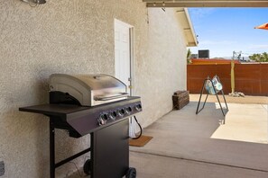 Un barbecue portatif doté d’un panneau de commande, installé sur une terrasse en béton, avec une maison en arrière-plan.