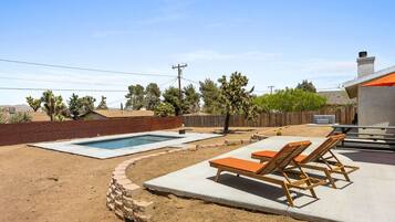 A backyard with a swimming pool, lounge chairs, and a barbecue area.
