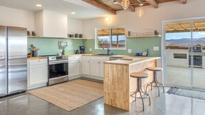 A modern kitchen with a wooden island, stainless steel appliances, and a view through the glass door.