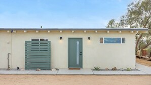 A single-story building with a green door, a window, and a small outdoor area with plants.