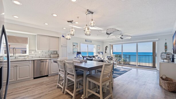 A modern kitchen with a dining area, large windows, and a view of the ocean.