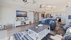 A modern living room with a sofa, coffee table, and a TV. There is a kitchen area with cabinets and a microwave.