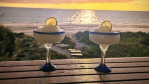 Two glasses of a dessert with a slice of lime on a wooden table overlooking a beach at sunset.