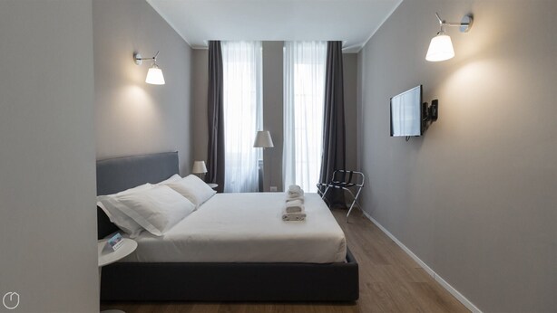 A modern hotel room with a large bed, a bedside table, a chair, and a TV mounted on the wall.