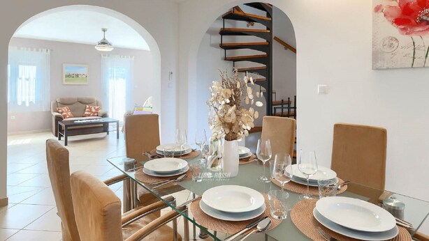 A dining area with a glass table set for four, surrounded by chairs. A staircase with a wooden railing is visible in the background. - Villa in Galizana With Bubble Bath (Vodnjan)