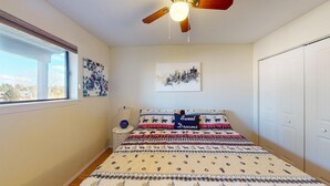 Une chambre à coucher avec un lit, un ventilateur de plafond, une fenêtre et des œuvres d’art accrochées aux murs.