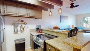 Une cuisine moderne dotée de plans de travail en granit, d’appareils électroménagers en acier inoxydable et de meubles en bois. On y trouve un coin repas avec une table et des chaises, ainsi qu’un ventilateur de plafond.