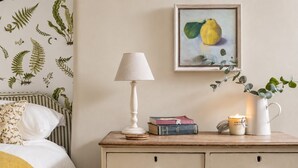 Ein Schlafzimmer mit einem Bett, einem Nachttisch mit Lampe, Büchern, einer Kerze und einem gerahmten Gemälde.