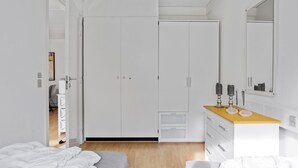 Une chambre moderne avec un placard, une coiffeuse avec un miroir et un lit avec une literie blanche.