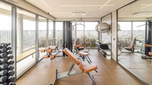 Une salle de sport moderne, équipée de matériel d’exercice, dotée de grandes fenêtres et offrant une vue sur l’extérieur.