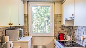 Eine kleine Küche mit Fenster, einer Mikrowelle, einem Toaster, einem Wasserkocher und einem Spülbecken.