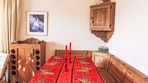 Ein Essbereich mit Holztisch, Stühlen und einer roten Tischdecke. Darüber befindet sich ein Holzschrank und an der Wand ein gerahmtes Bild.