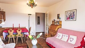 Ein gemütliches Wohnzimmer mit einem roten Sofa, Holzstühlen, einem Esstisch mit roter Tischdecke, einer Chandelier und einem Bücherregal.