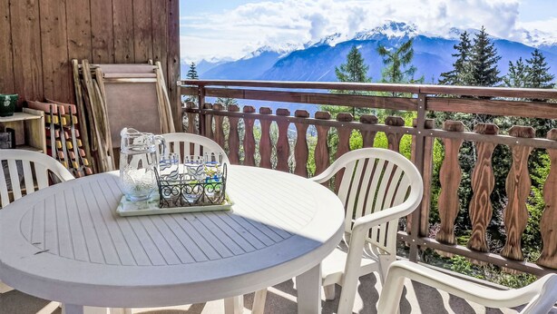 Eine Holzterrasse mit einem weißen Tisch und Stühlen mit Blick auf ein Gebirge.