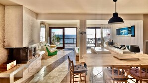 A spacious living area with a large window overlooking the sea, a dining area with a wooden table and chairs, and a cozy seating area with a green sofa and a fireplace. - Seaside apartment - Cap Ferret - Bassin d' Arcachon (Lège-Cap-Ferret)