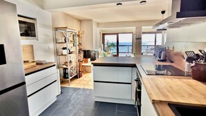 A modern kitchen with a view of the sea, featuring a central island, white cabinetry, and a large window. - Seaside apartment - Cap Ferret - Bassin d' Arcachon (Lège-Cap-Ferret)