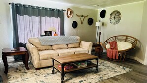 A living room with a sofa, coffee table, and a chair. There are hats on the wall and a guitar in the corner.