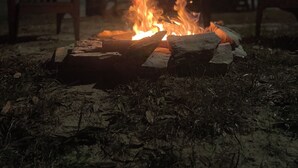 A campfire with chairs and tables in the background.
