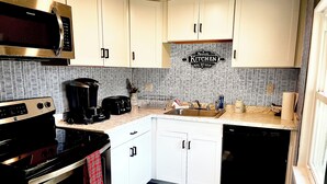 A compact kitchen with white cabinets, a stainless steel microwave, a coffee maker, and a dishwasher.