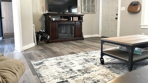 A living room with a fireplace, a television mounted above it, a wooden coffee table, and a patterned rug.