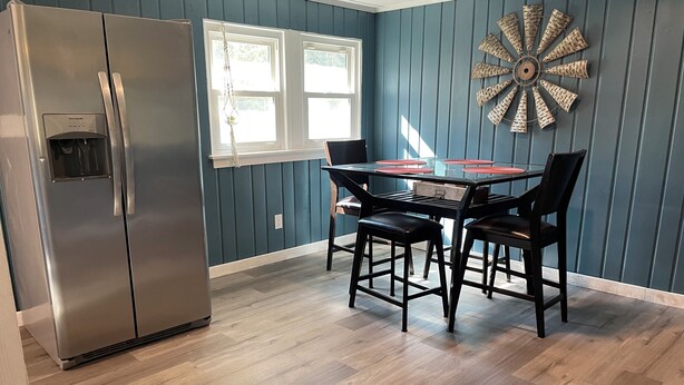 A kitchen with a stainless steel refrigerator, a dining table with four chairs, and a decorative wall piece.
