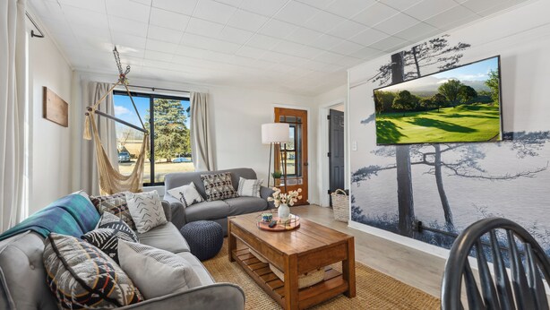 A living room with a grey sofa, wooden coffee table, and a large TV screen displaying a golf course.