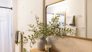 A bathroom with a mirror, a vase with flowers, a candle, and a towel rack.