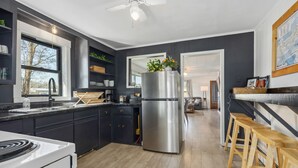 A modern kitchen with dark cabinetry, a stainless steel refrigerator, wooden stools, and a large window.