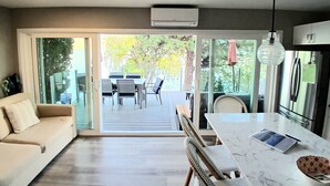 A modern kitchen with a marble countertop, a dining area with wicker chairs, a sofa, and a sliding glass door leading to an outdoor patio with a table and chairs.