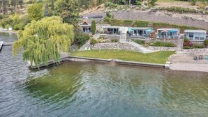 A lakeside property with a grassy lawn, a dock, and several modern houses with large windows.