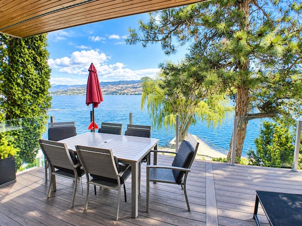 An outdoor deck with a table and chairs, overlooking a body of water and hills.