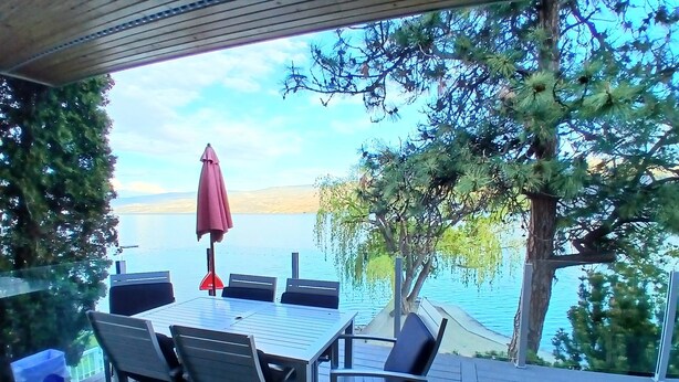 An outdoor deck with a table and chairs, overlooking a body of water and distant land.
