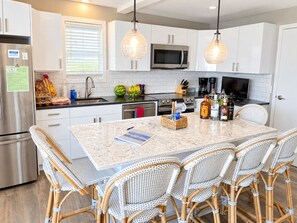 A modern kitchen with white cabinets, a stainless steel refrigerator, a microwave, and a dining area with wicker chairs.