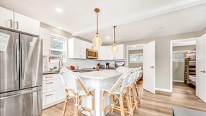 A modern kitchen with a central island, stainless steel refrigerator, and wicker chairs.