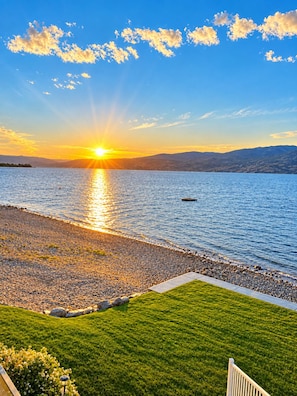 A sunset over a calm lake with a grassy area and a pathway leading to the water.